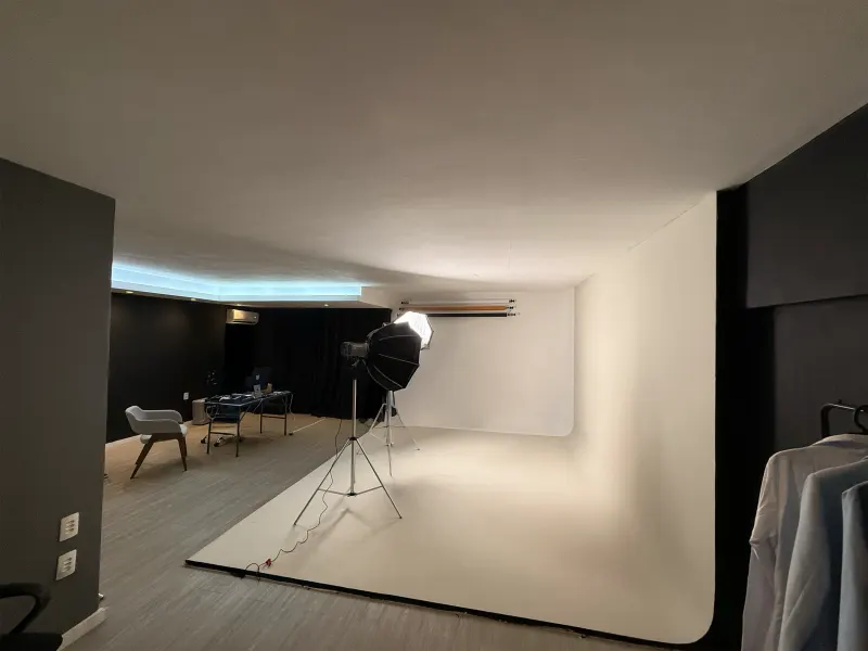 Visão geral do estúdio: fundo infinito em L, refletores, cadeiras e a mesa de reunião ao fundo